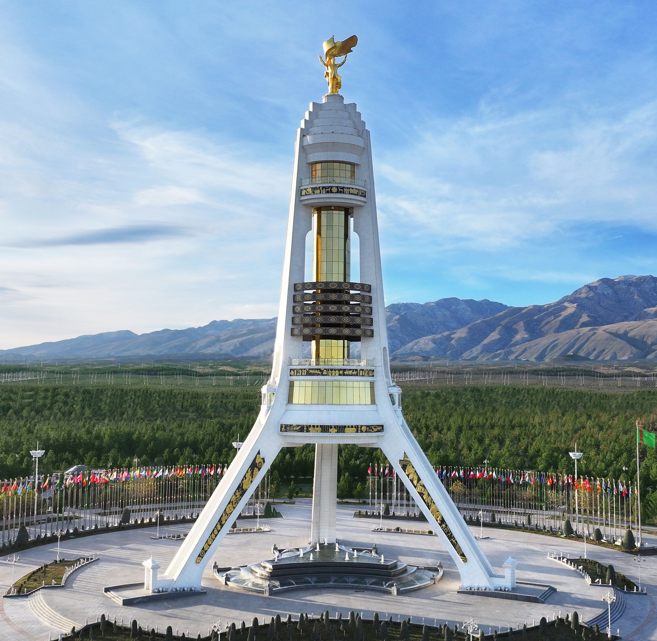 White marble Neutrality Monument with golden statue on top in Ashgabat, mountains background transit tour Turkmenistan